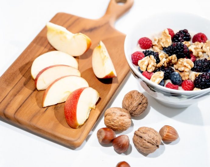 A vibrant breakfast bowl with mixed berries, walnuts, and apple slices on a rustic board.