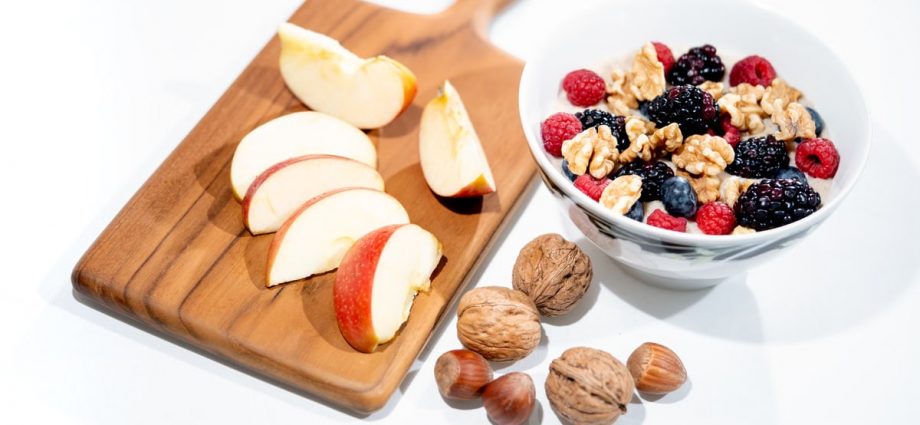 A vibrant breakfast bowl with mixed berries, walnuts, and apple slices on a rustic board.
