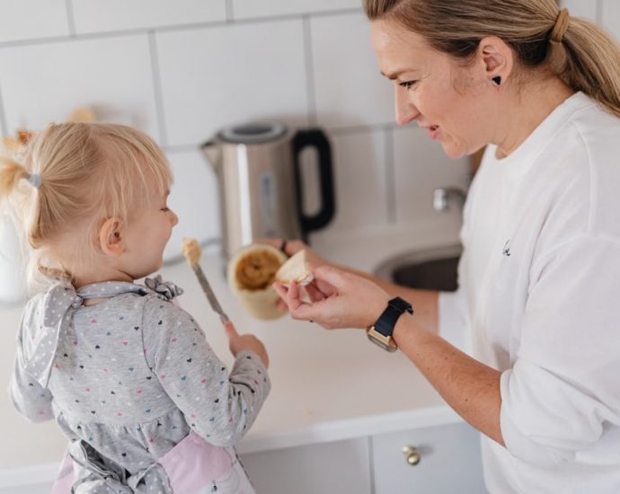 A mother and her young daughter interact while preparing food in a modern kitchen.