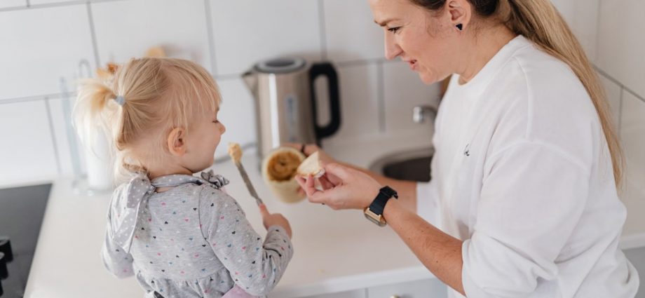 A mother and her young daughter interact while preparing food in a modern kitchen.